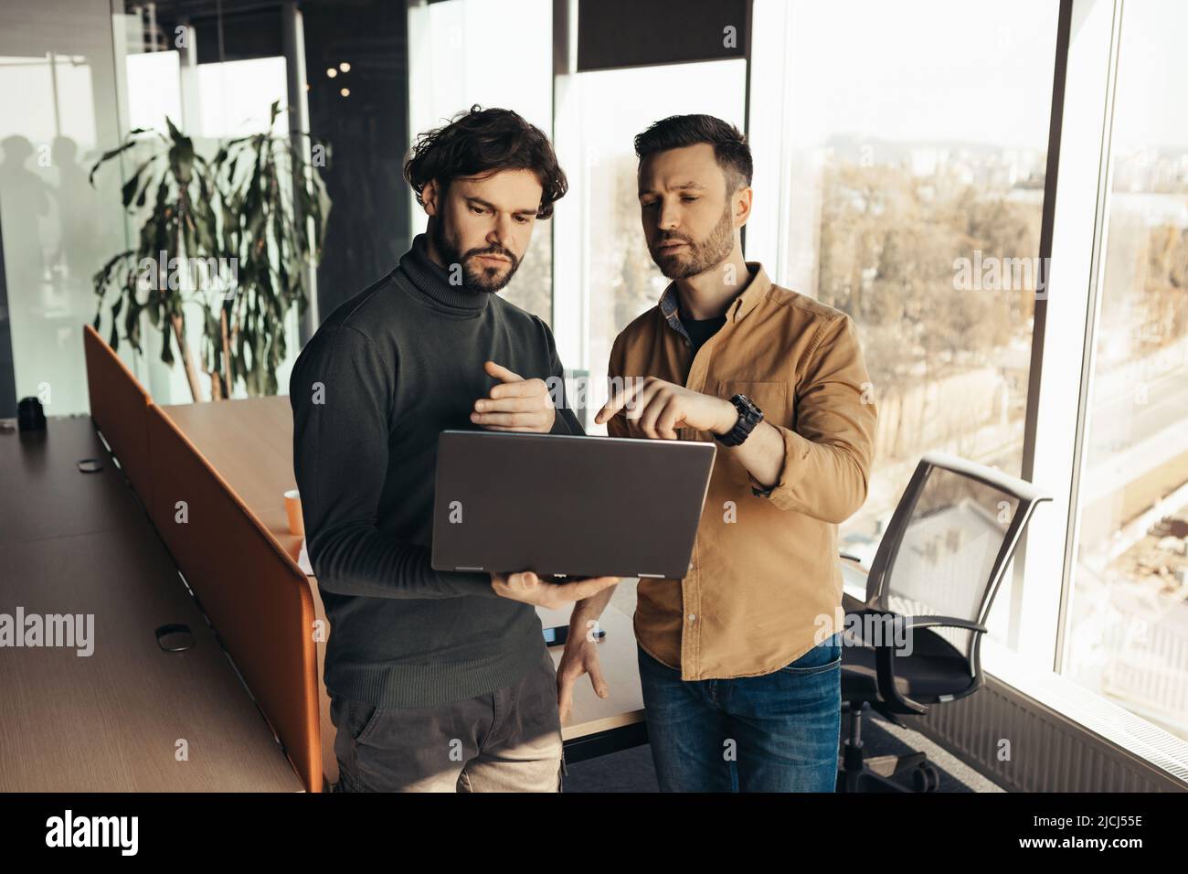 Colleghi di sesso maschile che lavorano insieme, utilizzando il computer moderno in un ufficio open space Foto Stock