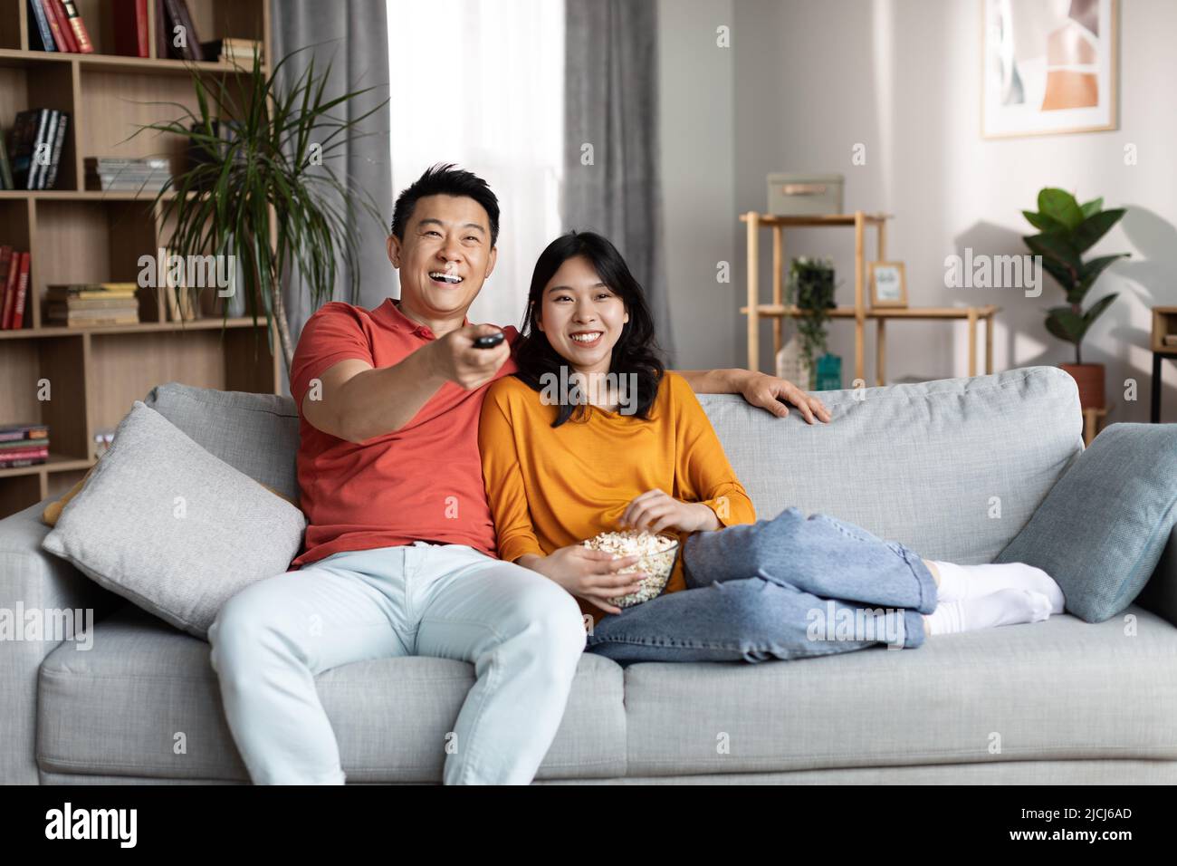 Amorevole coppia cinese che riposa sul divano, guarda la TV e ride Foto Stock