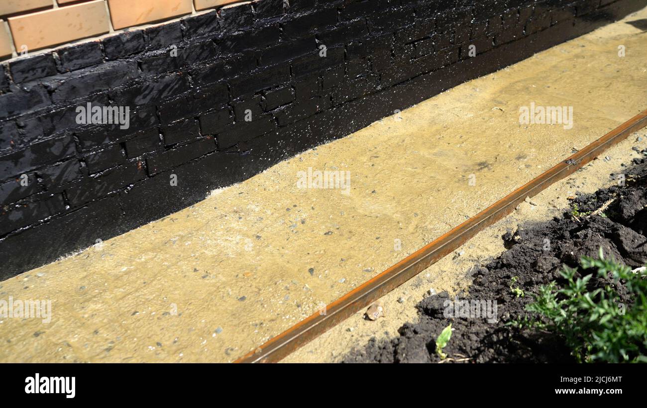 La sabbia è versata con acqua per stendere le lastre di pavimentazione. Il processo di posa di lastre di pavimentazione. Umidificazione della sabbia per pavimentazioni. Sabbia è versata da un tubo Foto Stock