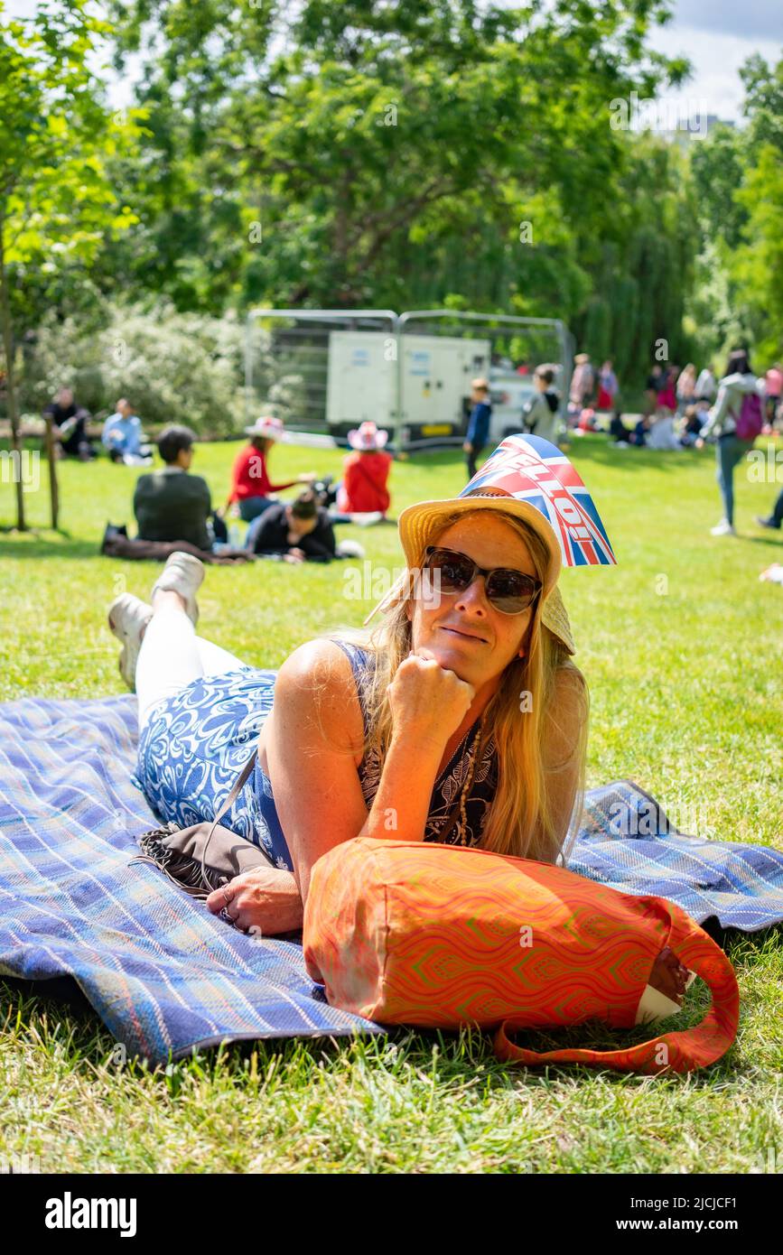 Donna con capelli biondi lunghi che si rilassa a St James Park sul Mall di Londra, Inghilterra durante la processione Platinum Jubilee. Foto Stock