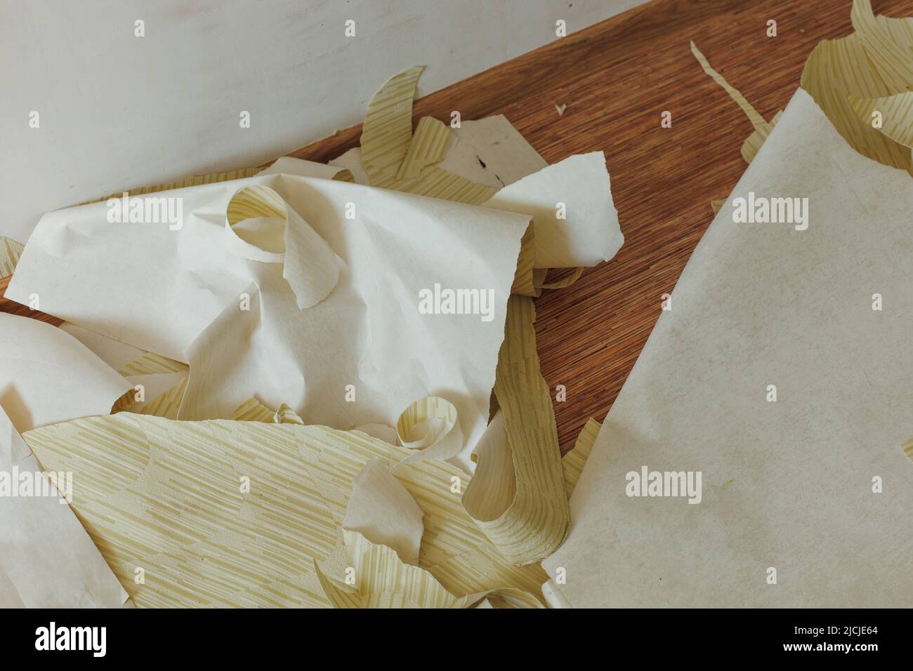 Pezzi strappati di carta da parati a strisce gialle gettati su pavimento di legno marrone in camera vuota. Scarti, stracci, ridecorazione domestica. Foto Stock