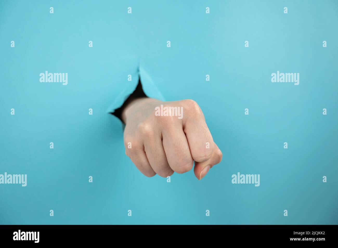 La mano di una donna che sporge da un buco da uno sfondo blu mostra un pugno. Foto Stock