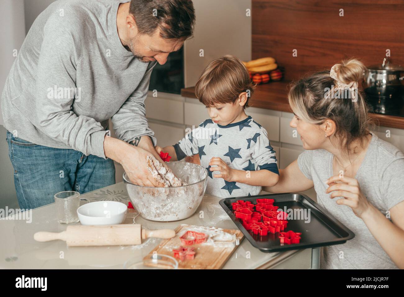 Papà, figlio e mamma sono impegnati a preparare biscotti in cucina a casa. Famiglia divertirsi insieme, hobby, lavoro di squadra. Persone felici. Foto Stock