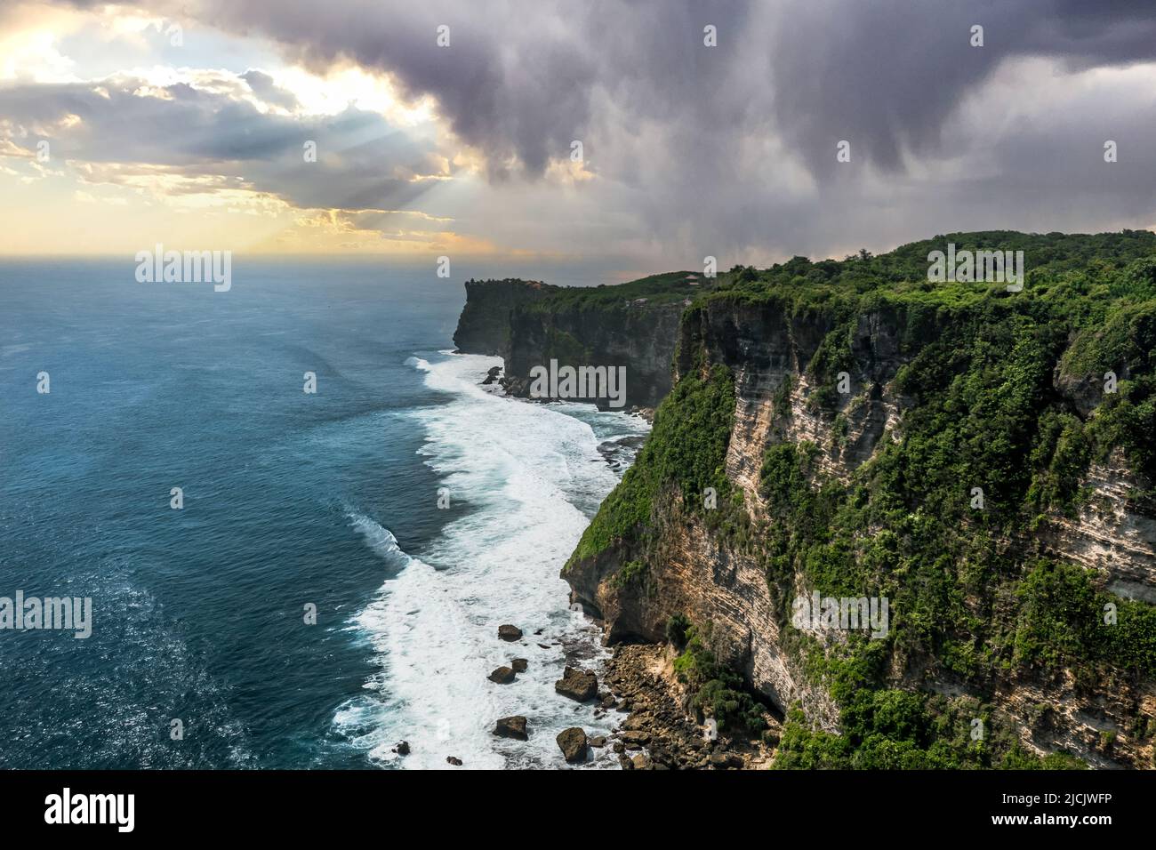 Antenna ad alta quota di grandi scogliere vicino alla spiaggia di Nyang Nyang a Uluwatu Bali Indonesia in un pomeriggio al tramonto con temporali e pioggia sul blu Foto Stock