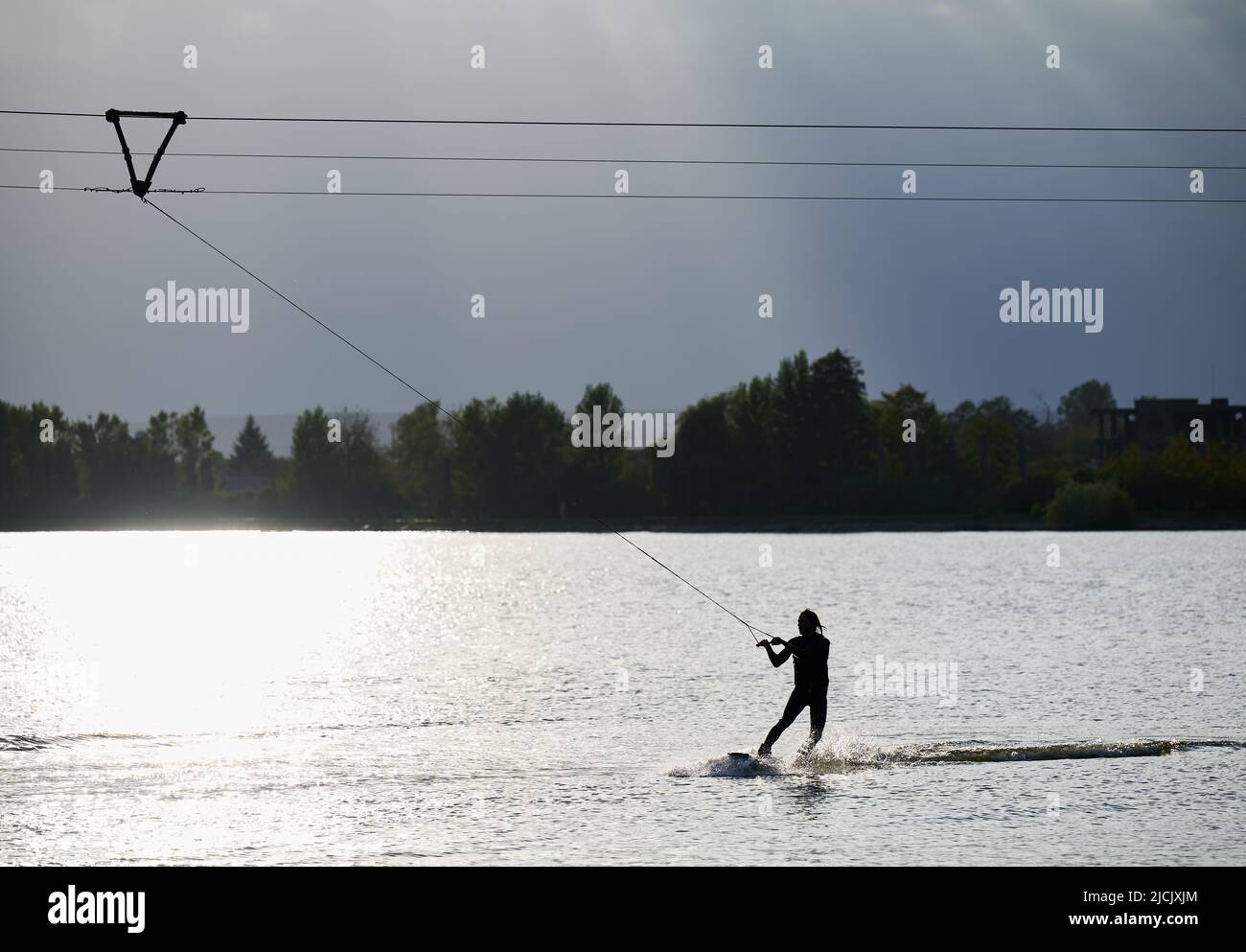 Silhouette di wakeboarder surf sul lago. Uomo atletico surfer divertirsi wakeboarding nel parco della funivia. Sport acquatici, attività all'aperto. Foto Stock