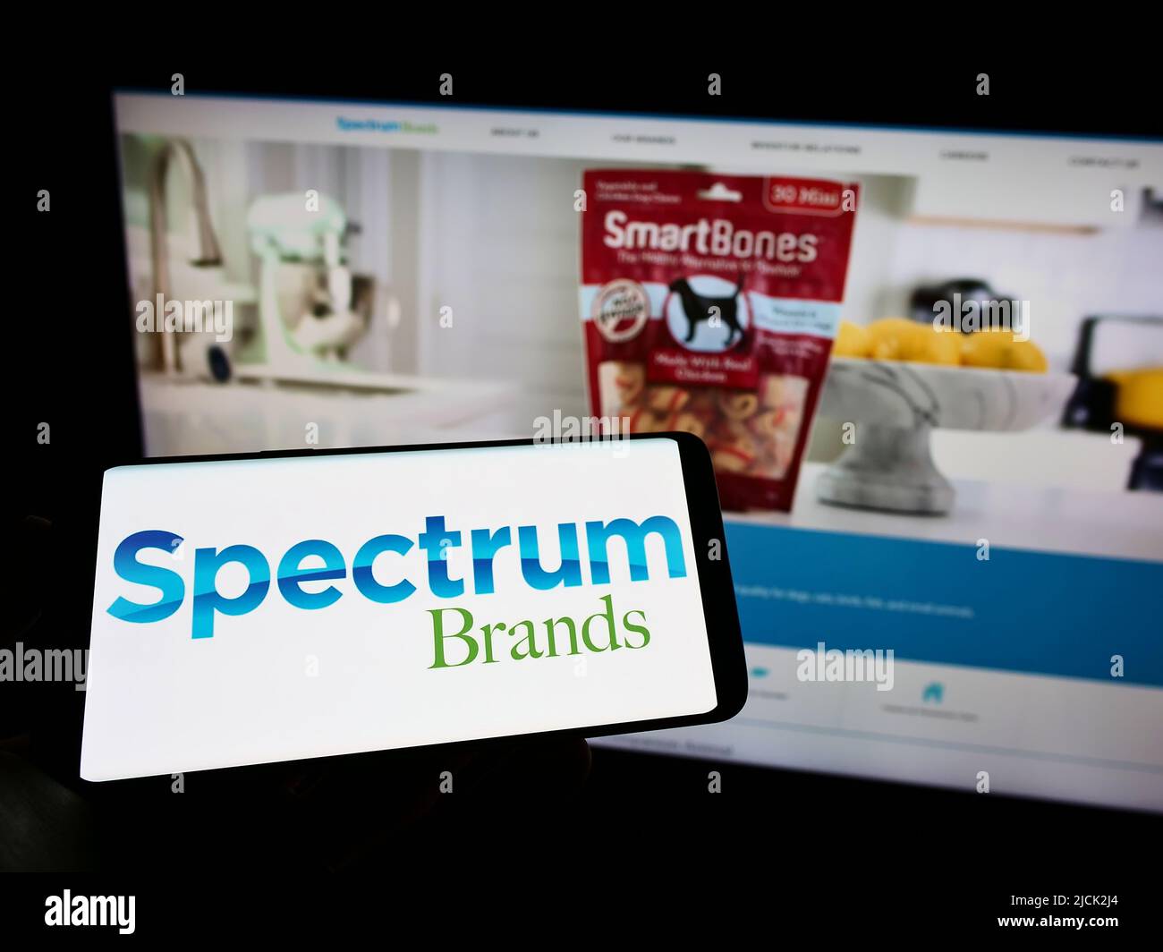 Persona che tiene uno smartphone con il logo della società statunitense Spectrum Brands Holdings Inc. Sullo schermo di fronte al sito Web. Mettere a fuoco sul display del telefono. Foto Stock
