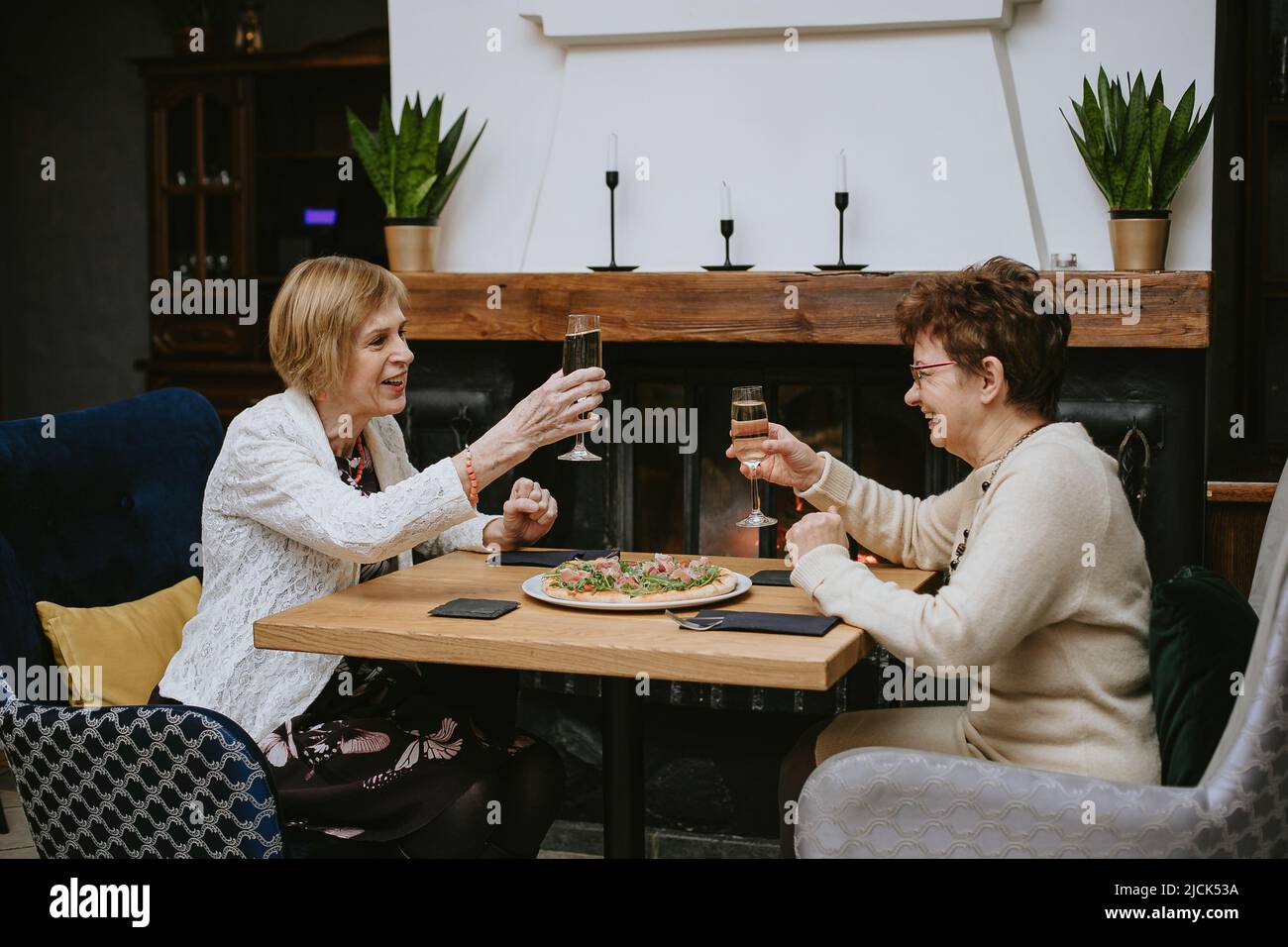 Due donne anziane che hanno cenato al ristorante, signora attraente che passa il tempo insieme all'interno. Vecchi amici che bevono vino in appartamento moderno. Foto Stock