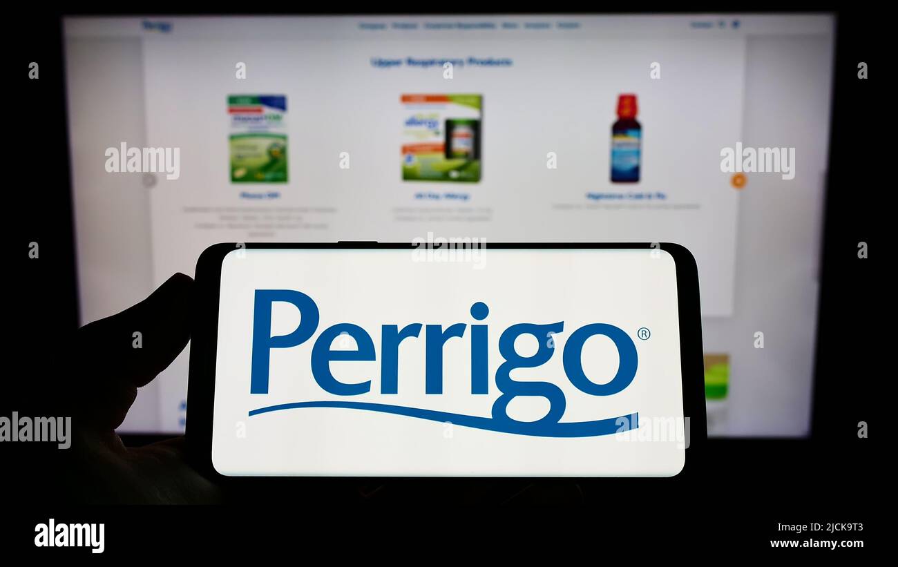 Persona che tiene uno smartphone con il logo del produttore farmaceutico Perrigo Company plc sullo schermo di fronte al sito web. Mettere a fuoco sul display del telefono. Foto Stock
