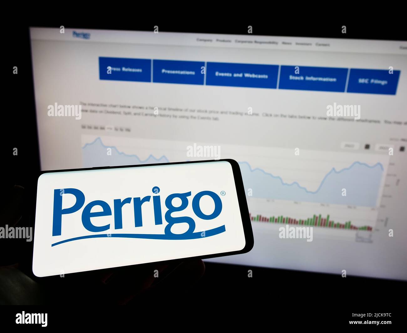 Persona che tiene il telefono cellulare con il logo del produttore farmaceutico Perrigo Company plc sullo schermo di fronte alla pagina web. Mettere a fuoco sul display del telefono. Foto Stock