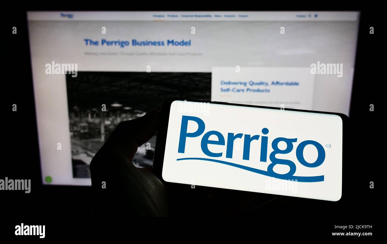 Persona che tiene il cellulare con il logo del produttore farmaceutico Perrigo Company plc sullo schermo di fronte al sito web. Mettere a fuoco sul display del telefono. Foto Stock