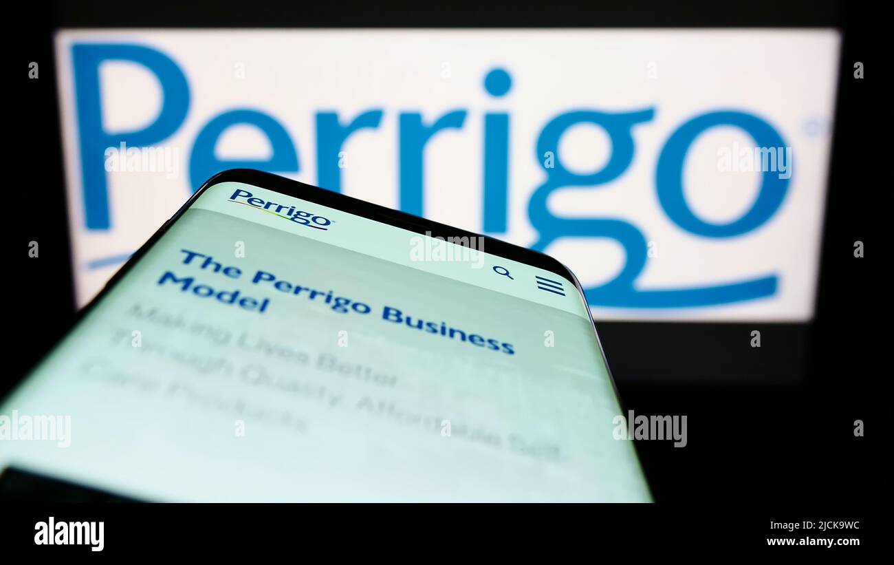 Smartphone con sito web del produttore farmaceutico Perrigo Company plc sullo schermo di fronte al logo. Mettere a fuoco sulla parte superiore sinistra del display del telefono. Foto Stock