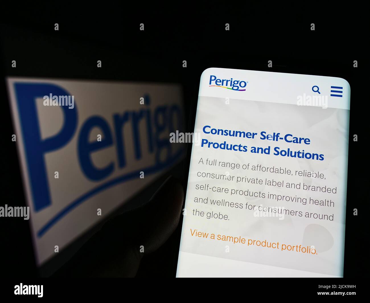 Persona che tiene il cellulare con pagina web del produttore farmaceutico Perrigo Company plc su schermo con logo. Concentrarsi sul centro del display del telefono. Foto Stock
