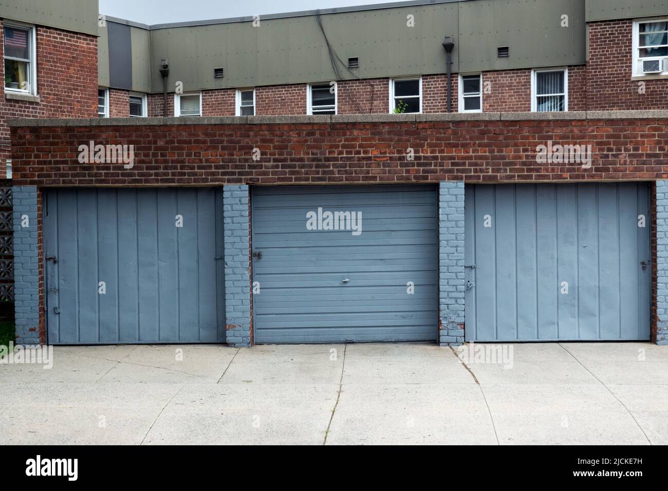 PAESAGGIO URBANO. Tre porte garage dipinte blu ciano con appartamenti a due piani sullo sfondo. Su Francis Lewis Boulevard a Queens, New York. Foto Stock