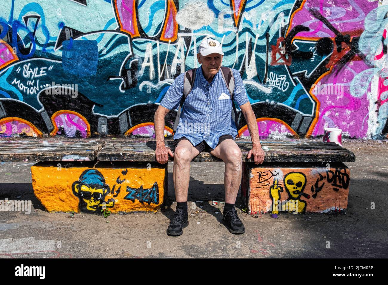 Uomo anziano seduto sul banco di fronte al lavoro di Street art sul muro di Berlino a Mauerpark, Prenzlauer Berg, Berlino, Germania Foto Stock