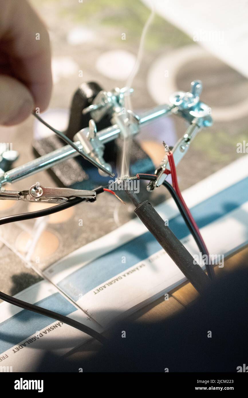Primo piano di macro di un uomo che fa lavoro di elettricità o che mette i fili insieme fondendo il piombo Foto Stock