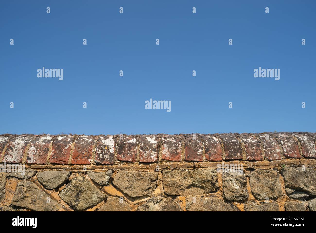 Ragstone di Kentish un calcare grigio duro usato per costruire un muro di confine forte con mattone rosso che si accoppa e lichen sulla parte superiore contro un cielo blu Foto Stock