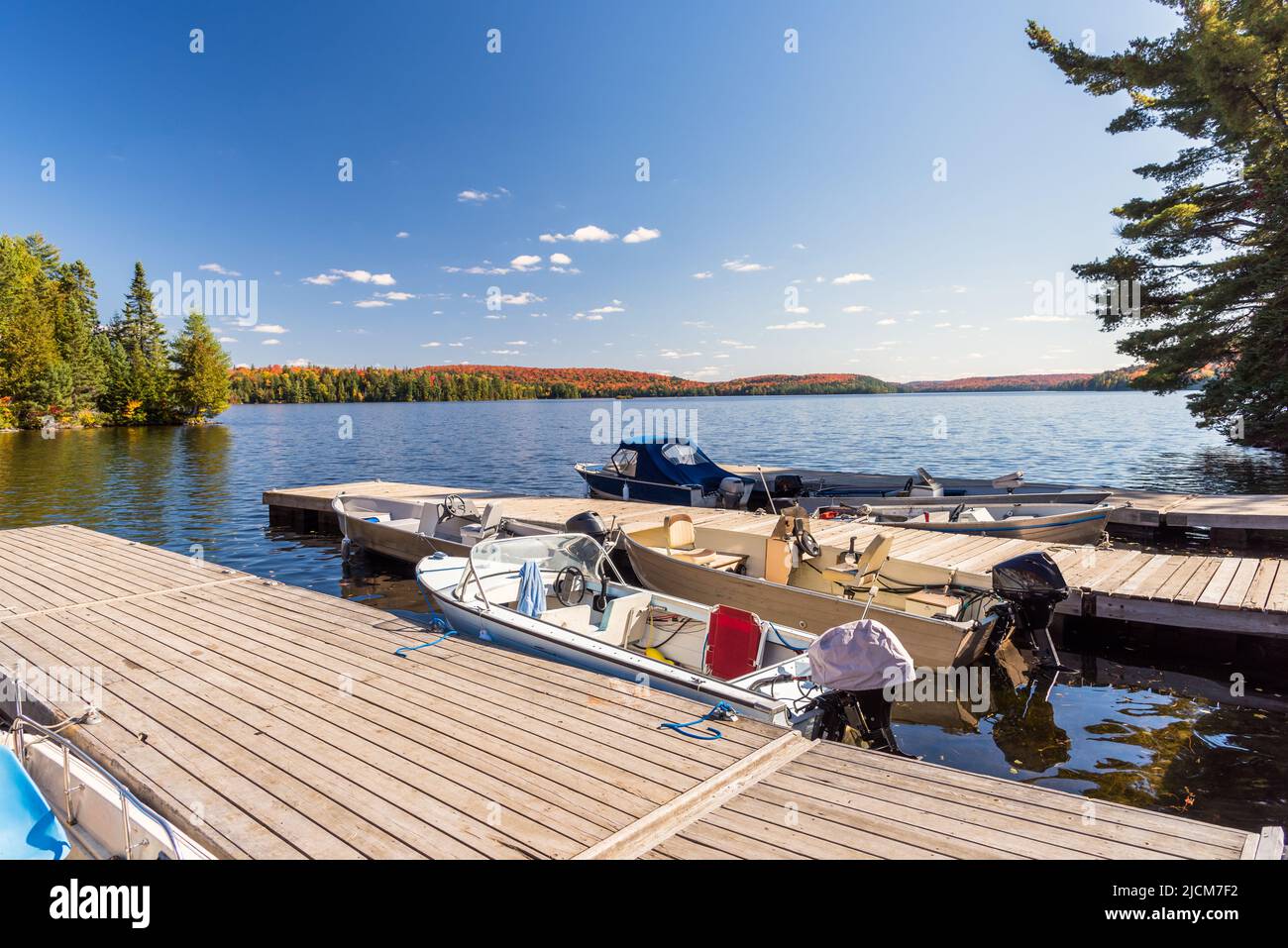 Barche in un piccolo porto su un bellissimo lago circondato da foresta al picco dei colori autunnali una giornata di sole. Foto Stock