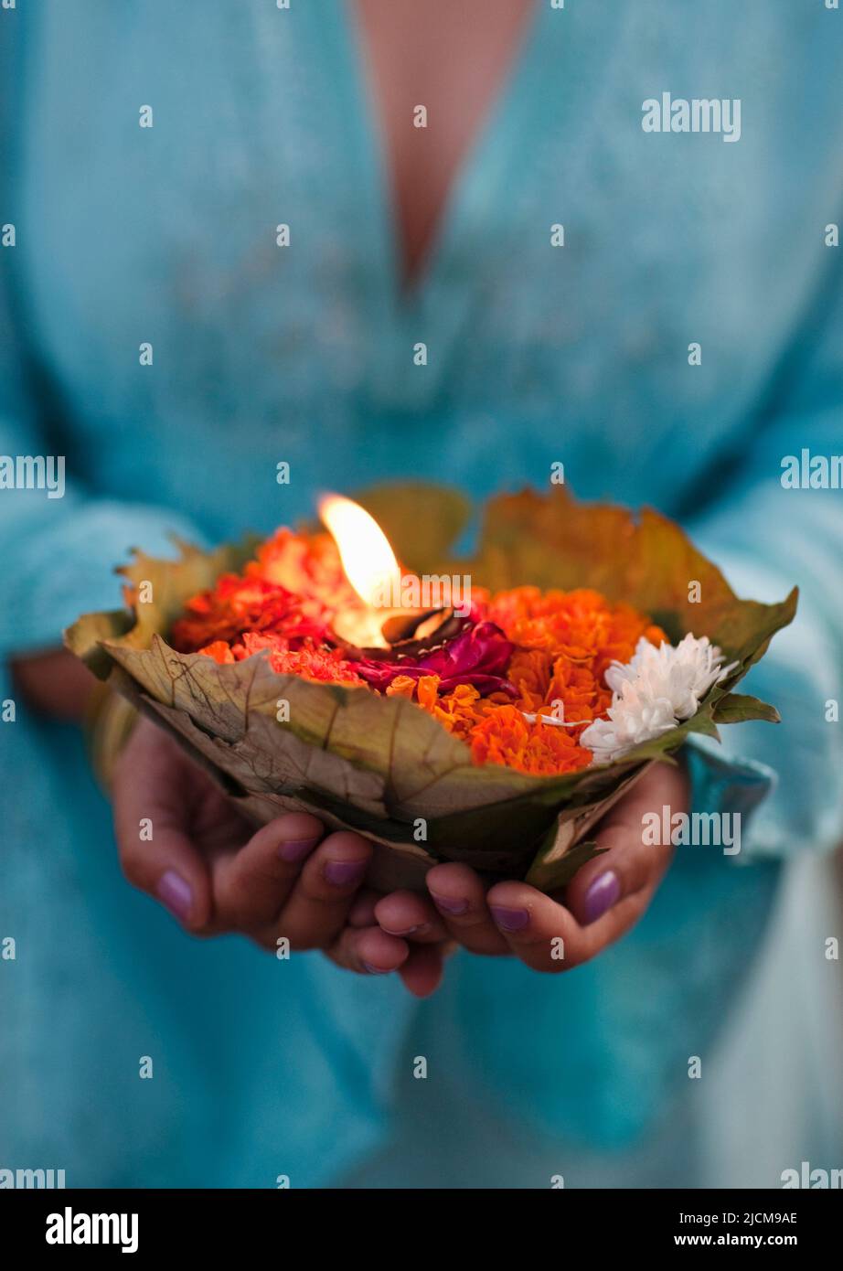 Una donna fa un'offerta floreale al fiume Ganges al tramonto a Rishikesh, Uttarakhand, India. Foto Stock