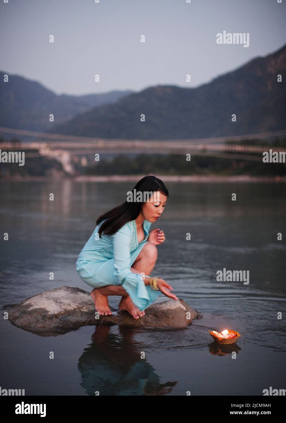 Una donna fa un'offerta floreale al fiume Ganges al tramonto a Rishikesh, Uttarakhand, India. Foto Stock