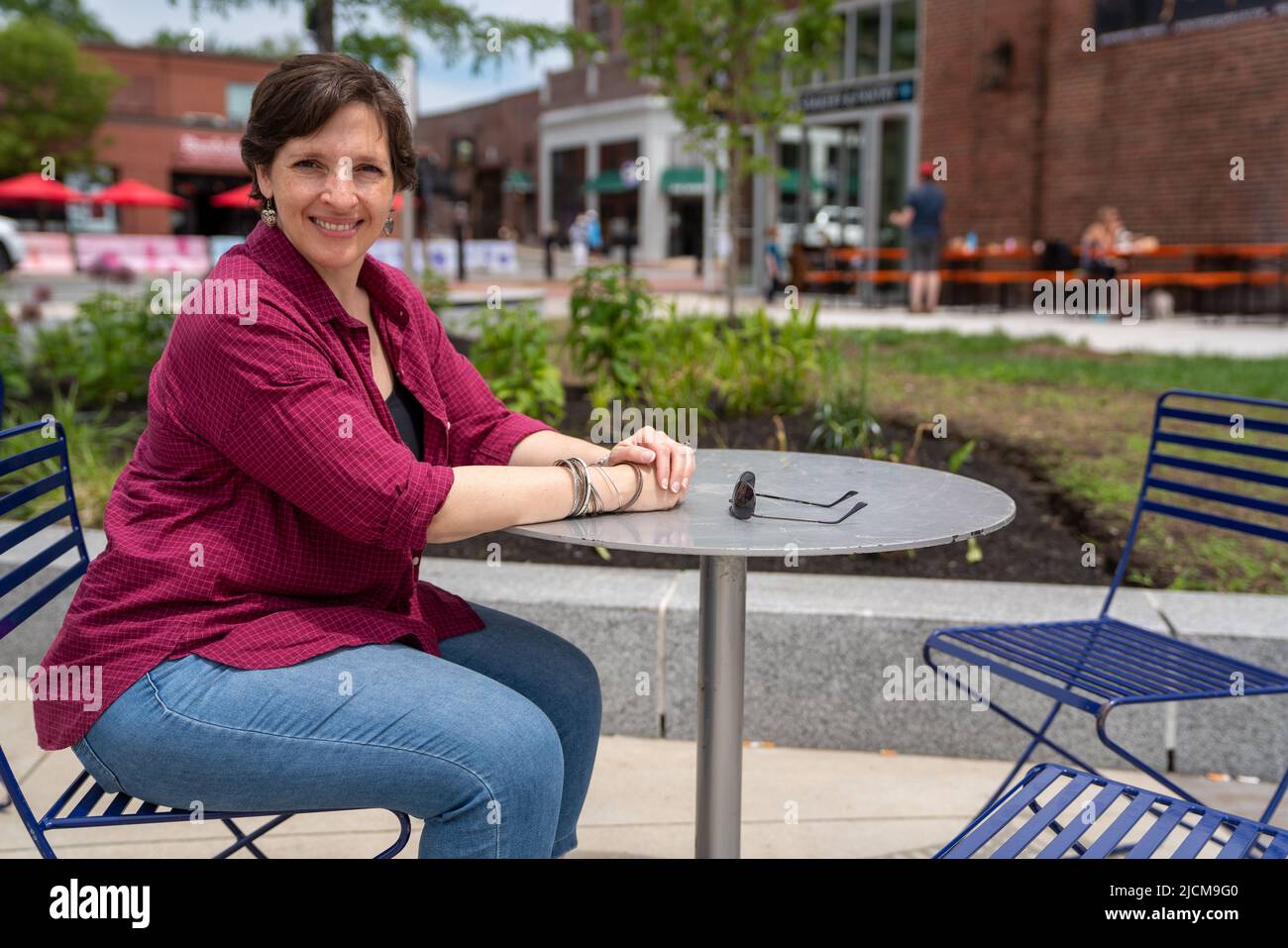 Felice, donna matura seduta ad un tavolo all'aperto da solo Foto Stock