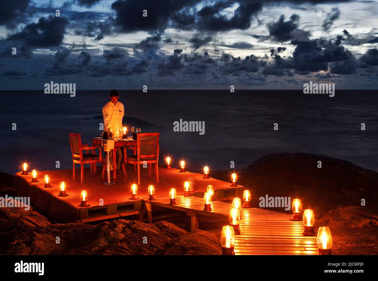 Un cameriere accende le candele e fissa un tavolo per due per una cena romantica sulla spiaggia. Aturuwella, Bentota, Sri Lanka. Foto Stock