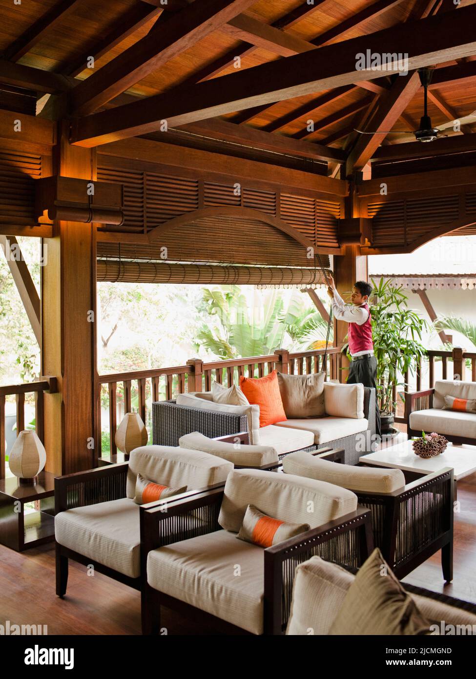 Un membro del personale dell'hotel attira le tende del salotto al secondo piano per lasciare la luce del mattino al la Residence d'Angkor, Siem Reap, Cambogia. Foto Stock