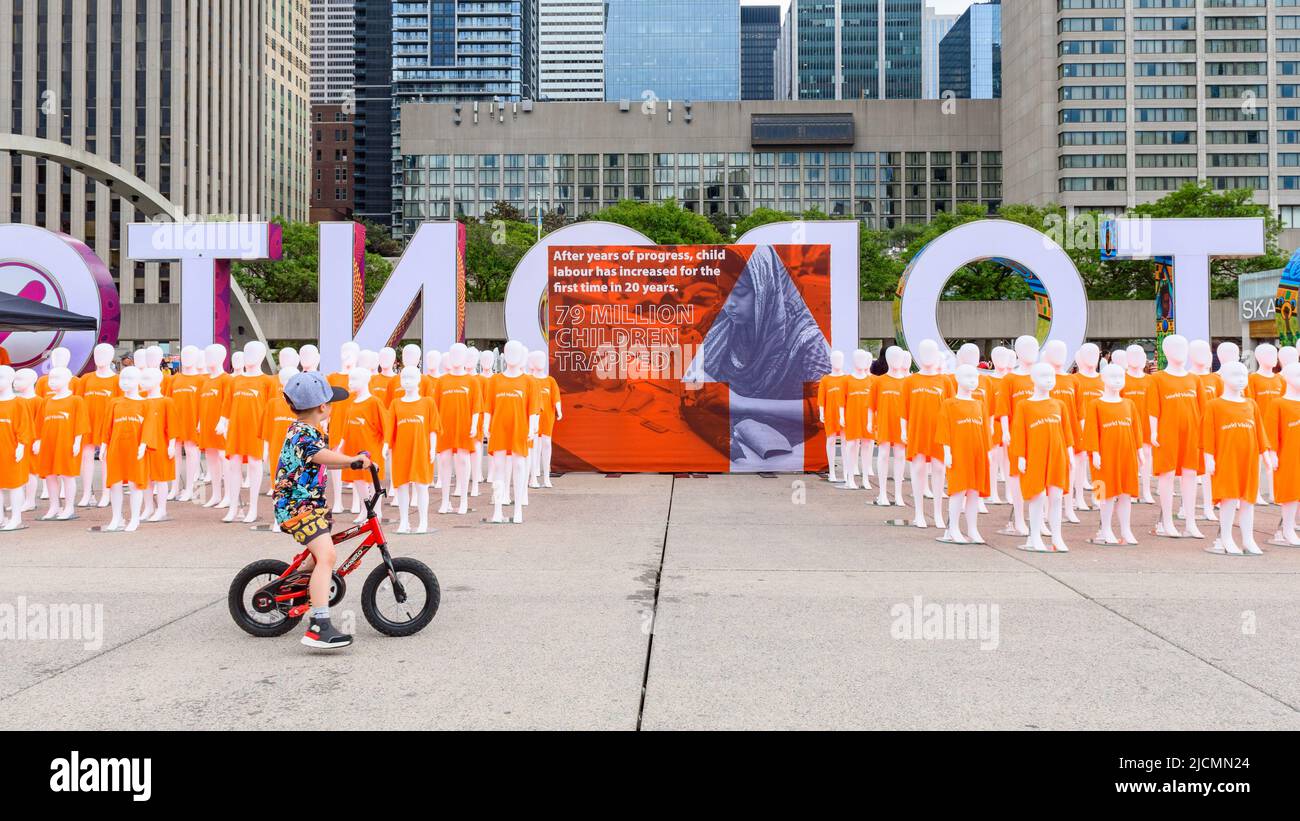 Un bambino corre una bicicletta da un pezzo d'arte di World Vision sta raccogliendo firme contro il lavoro minorile. Foto Stock