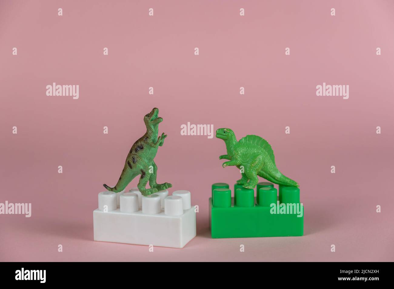 Dinosauri in miniatura su due blocchi di costruttori per bambini. Due piccole miniature verdi di dinosauri predatori in piedi sulle loro gambe posteriori. P Foto Stock