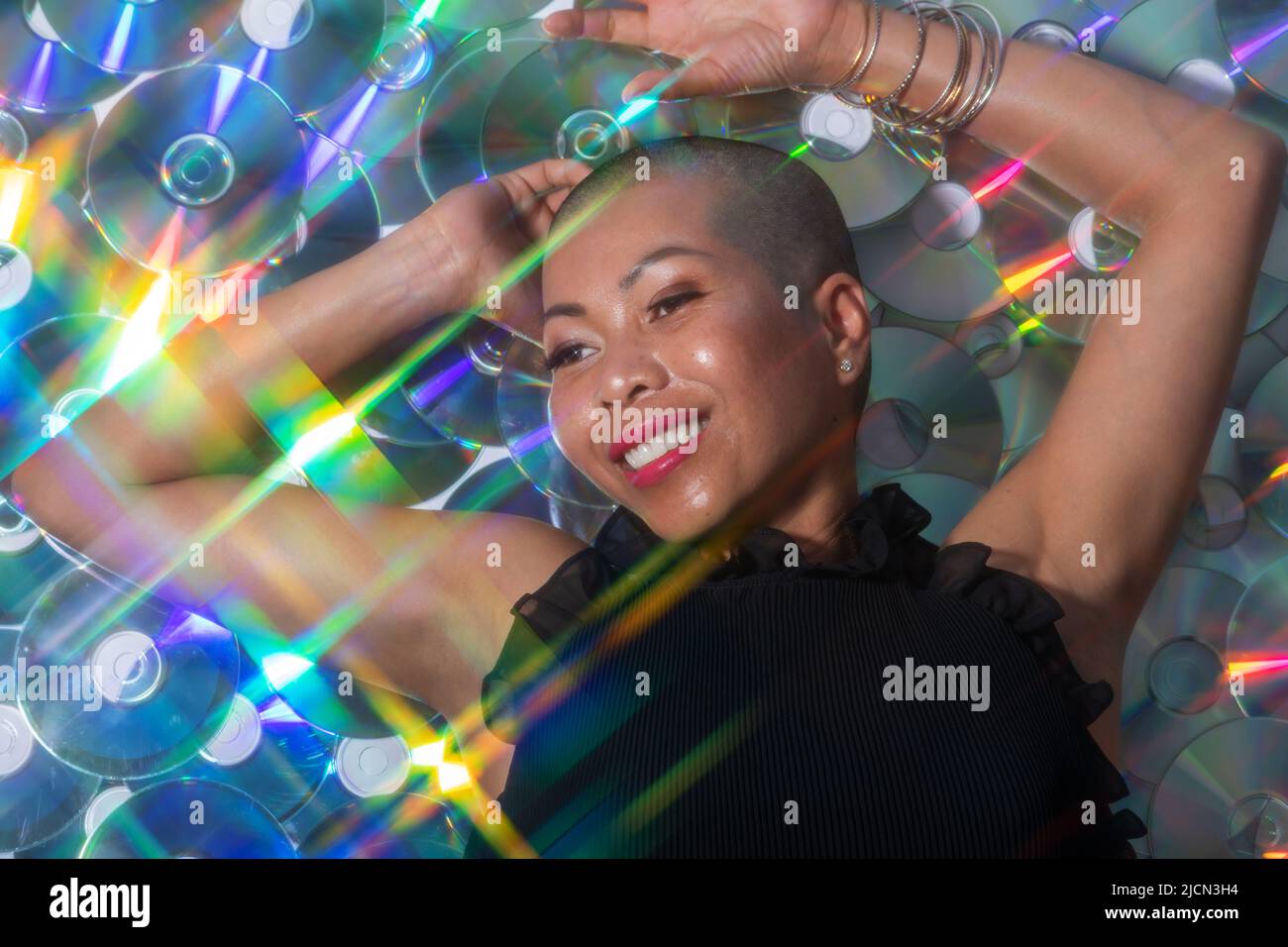 Divertimento e musica concetto. Ritratto di bella e felice con sorriso Thai donna sdraiata su compact disc sfondo. Modello illuminato con lucida e. Foto Stock