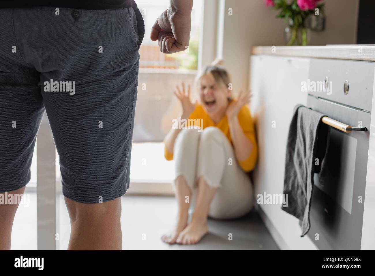 coppia in problemi con la violenza, marito o uomo che attacca e minaccia moglie donna urlando nella paura seduta sul pavimento in cucina Foto Stock