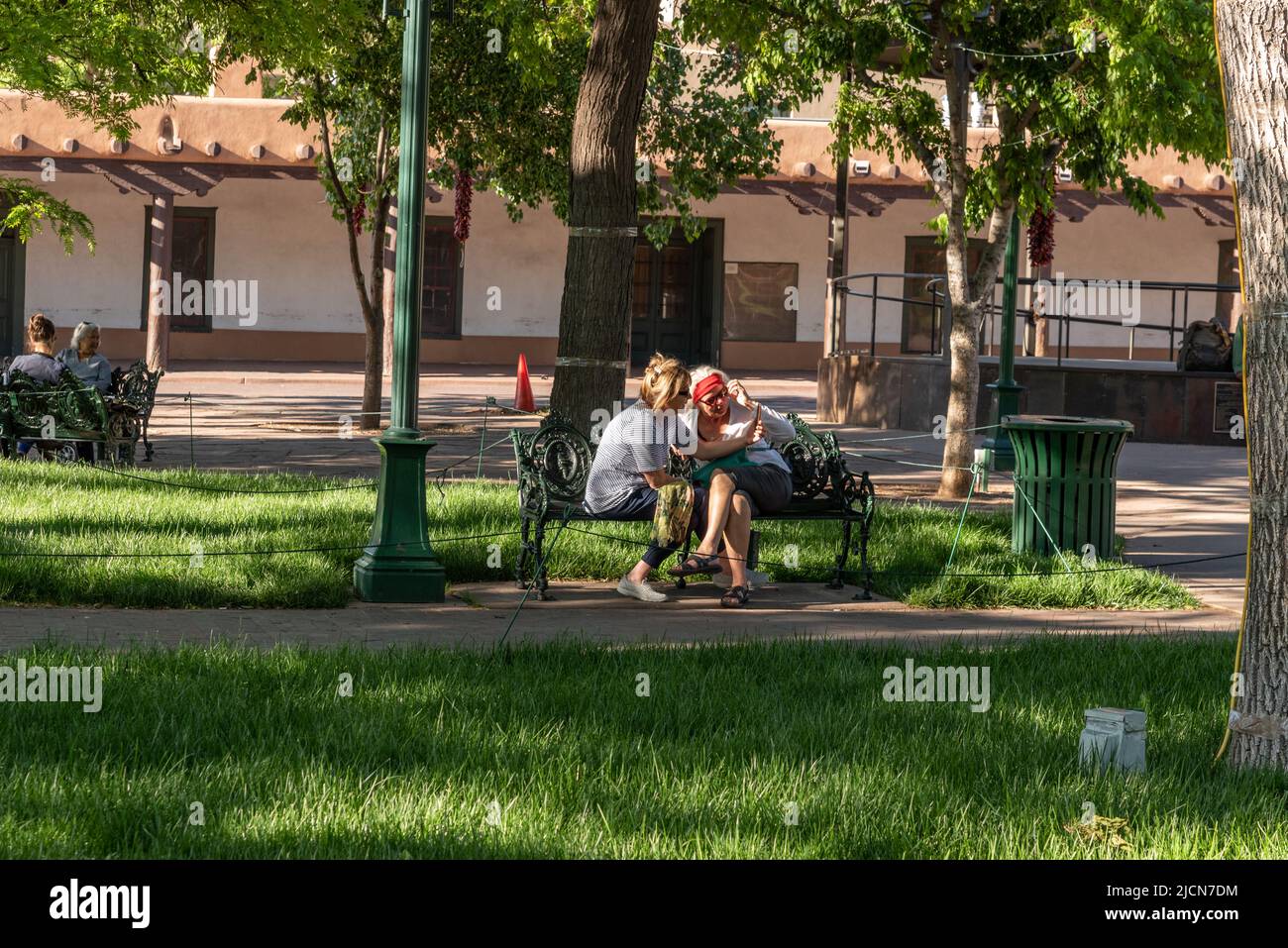 Due donne si riuniscono su una panchina del parco mentre parlano su un telefono con un altoparlante nel Santa Fe Plaza Park, Santa Fe, New Mexico. Foto Stock