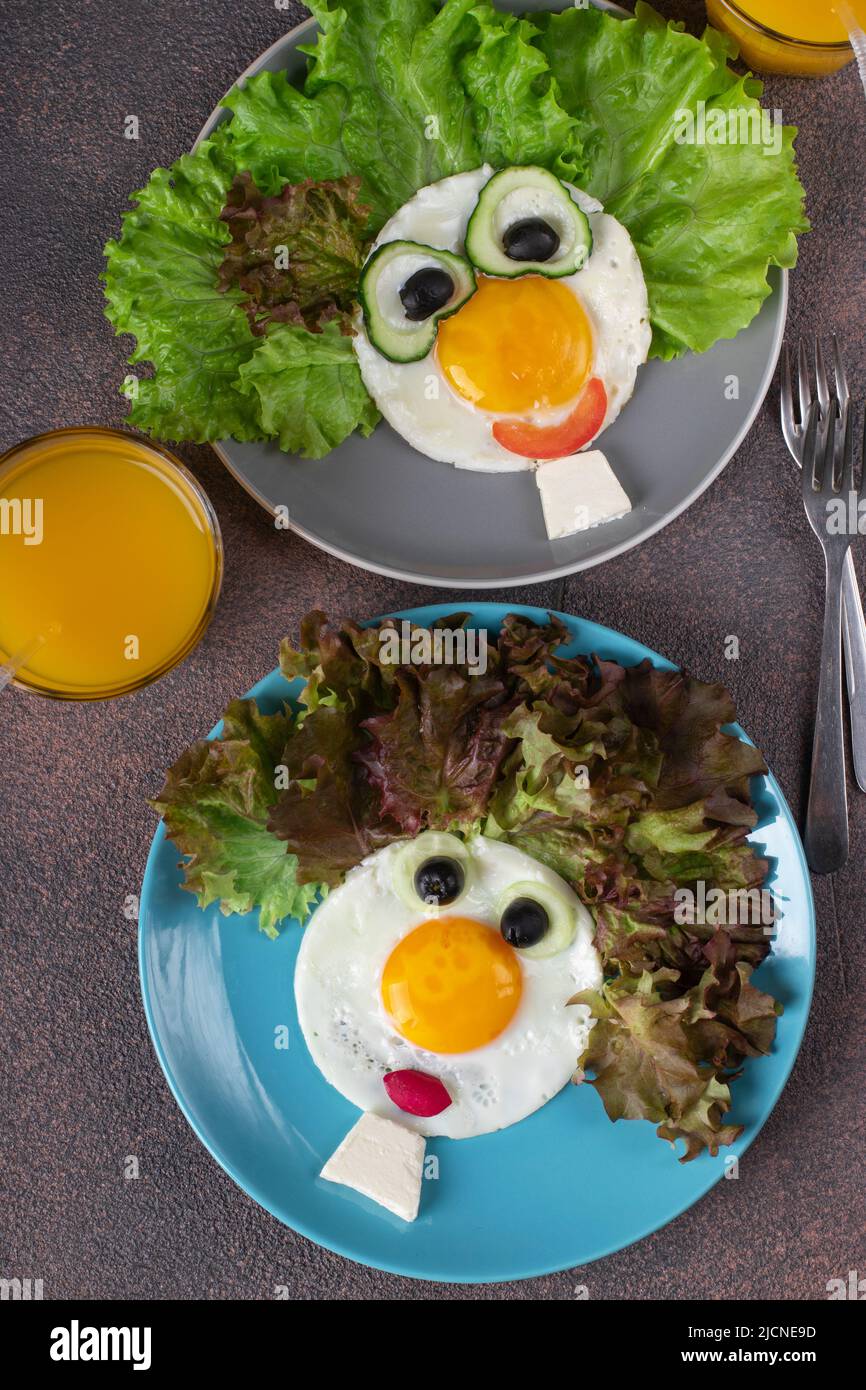 Fun Food for Kids - faccine sorridenti a base di uova fritte, cetrioli, pomodori, ravanelli, olive nere e foglie di lattuga su due piatti. Creativo sano Foto Stock