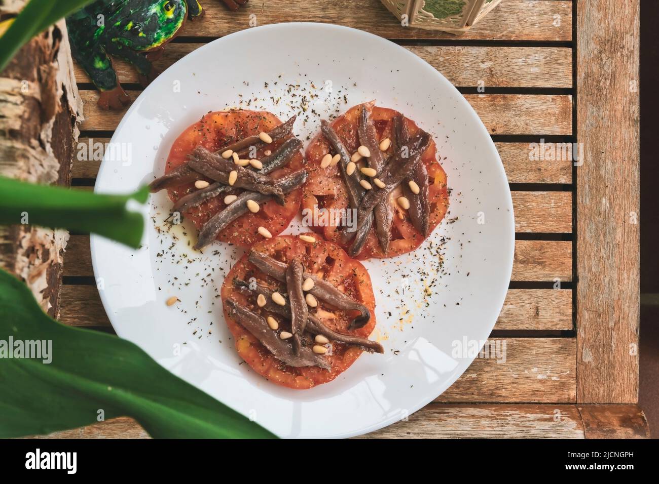 Fette di pomodoro organico ricoperte di acciughe e pinoli su un tavolo di legno di teak Foto Stock