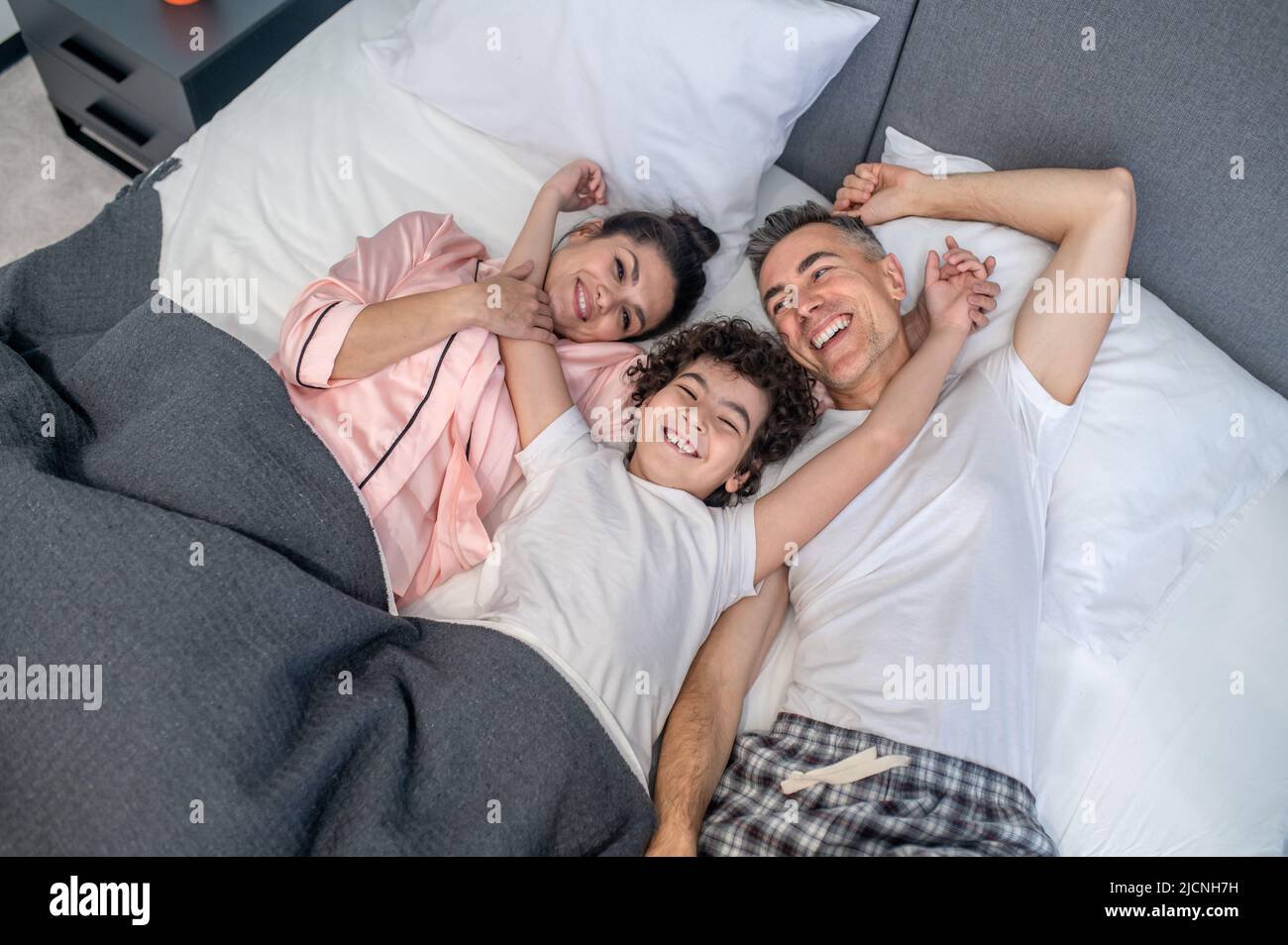 Una famiglia carina che sta nel letto sorridendo e sembrando cheeful Foto Stock
