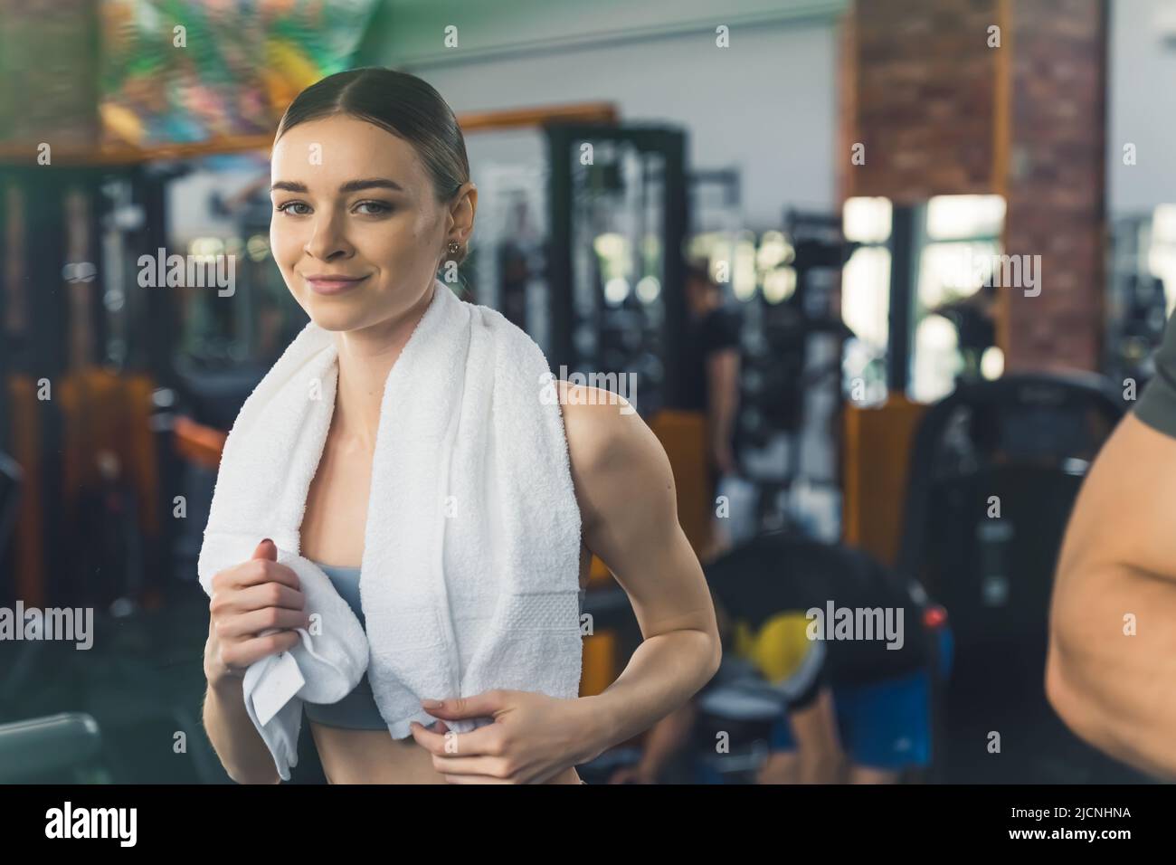 Ritratto interno palestra di una giovane donna caucasica sorridente con un asciugamano bianco sulle braccia. Foto di alta qualità Foto Stock