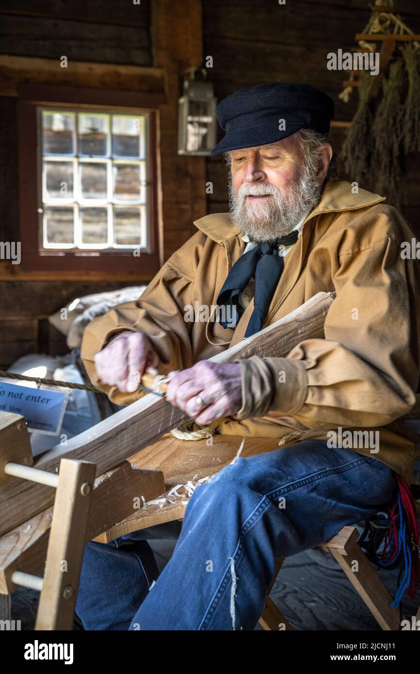 Storico in costume e attore di rievocazione intagliando legno a Fort Nisqually, Tacoma, Washington Foto Stock