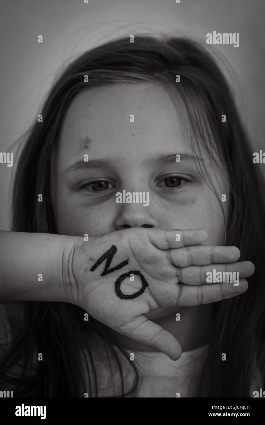 Ritratto bianco e nero di piccola ragazza livida che alza la mano per coprire la bocca, mostrando l'iscrizione no sul palmo. Verticale. Foto Stock