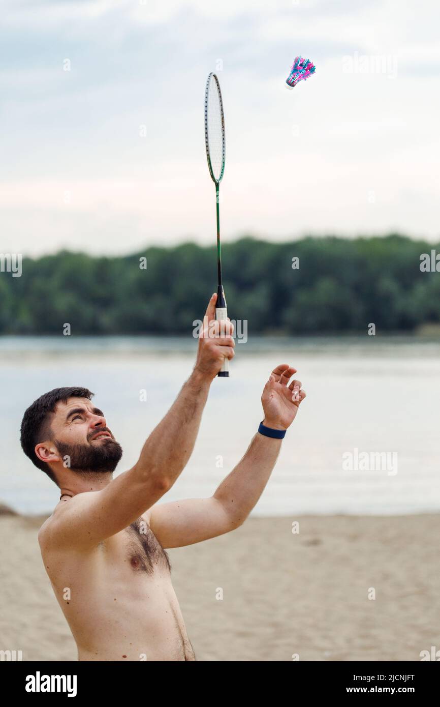 Vista laterale dell'uomo nudo senza peli di mezza età con capelli corti e scuri che giocano a badminton su sfondo cielo. Estate. Foto Stock