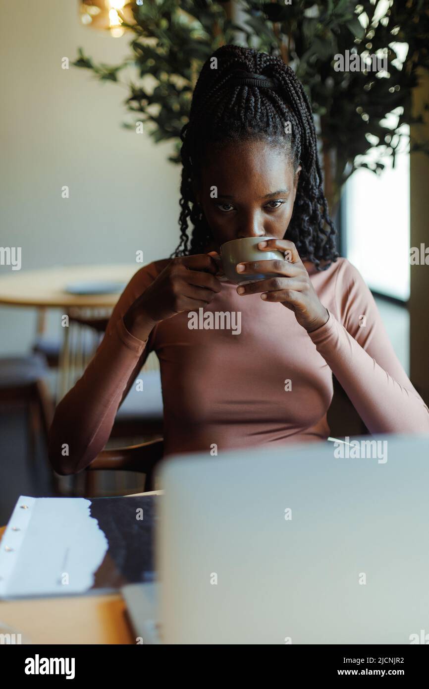 Verticale multirazziale afro americano pelle scura donna, bere gustoso caffè cappuccino. Prendetevi una pausa sul lavoro freelance remoto Foto Stock