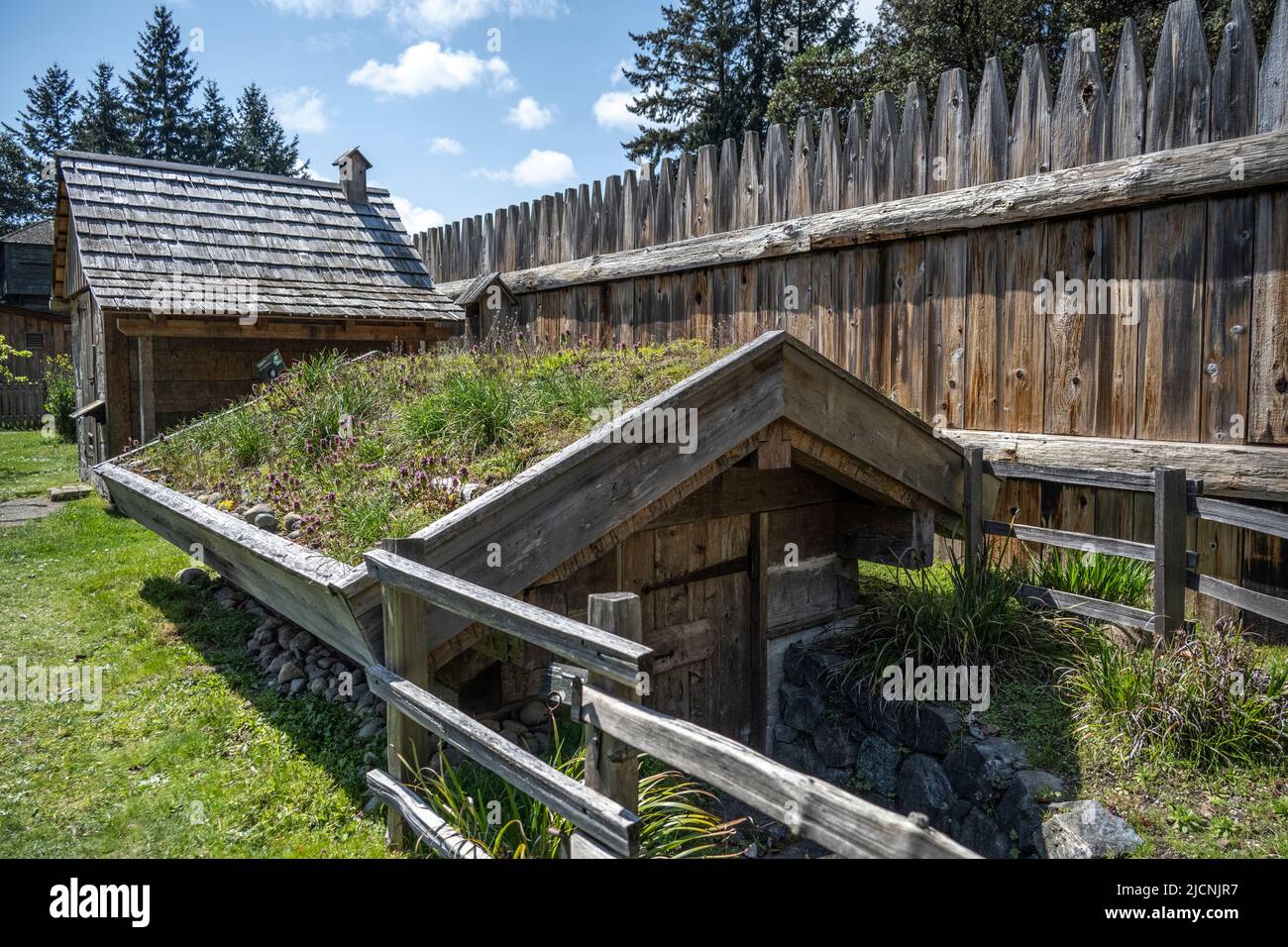 Edificio adibito a deposito di patate durante l'estate con la casa fumaria sullo sfondo presso il Fort Nisqually Living Museum di Tacoma, W. Foto Stock