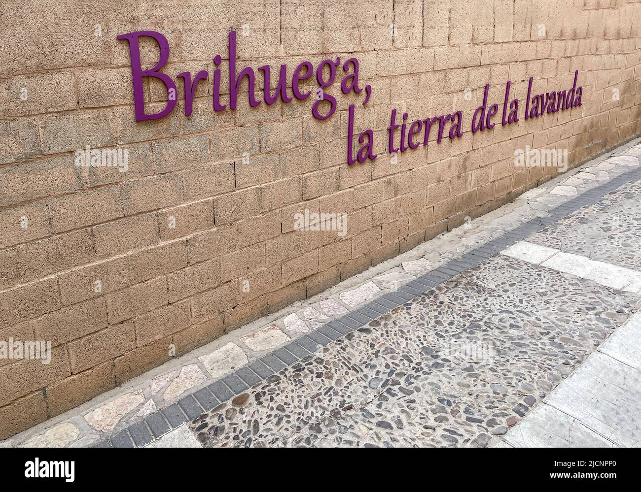 Un muro di mattoni chiaro con lo slogan spagnolo Brihuega la terra di lavanda, festa o fiera di lavanda, su una strada lastricata medievale a Brihuega, Spagna Foto Stock