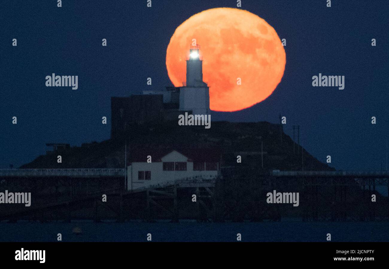 La Luna piena di fragole raffigurata dietro la testa di mumbles a Swansea, Galles, mentre la Supermoon si innalza nel cielo della sera. È la sesta luna piena dell'anno, ma come è una superluna, appare più grande e più luminosa nel cielo della sera. Foto Stock