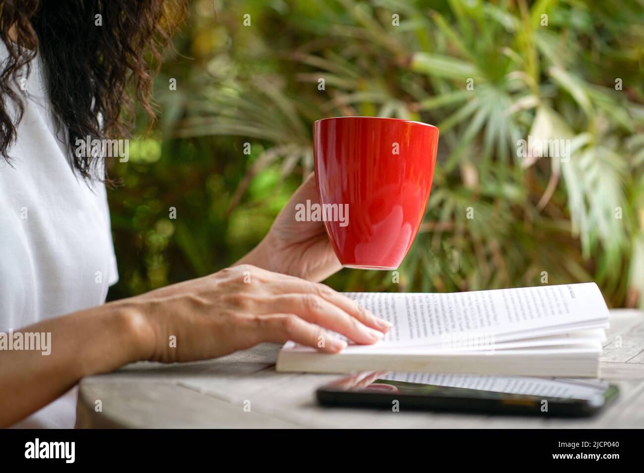 Donna che ha una tazza di caffè e leggere un libro, primo piano. Concetto di cura di sé o di lettura per il tempo libero. Foto Stock