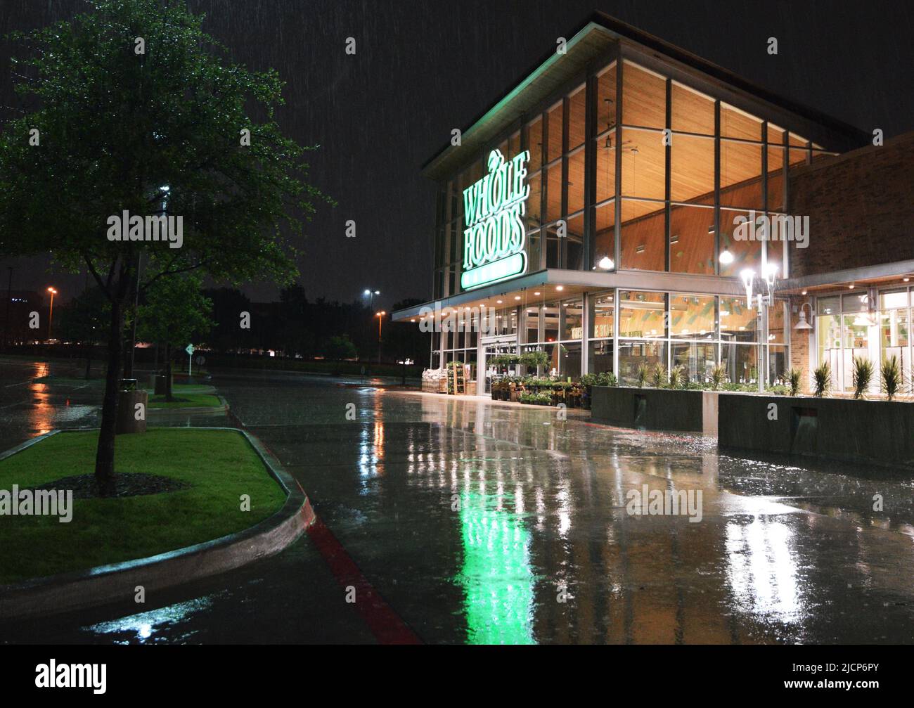Le luci verdi di un cartello Foods Market intero si riflettono nel parcheggio in una notte piovosa Foto Stock