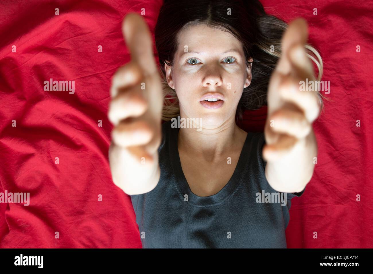 La ragazza si trova in un letto su un foglio rosso e allunga le braccia fino alla cima, dormire e riposare a casa a letto, comfort e intimità Foto Stock