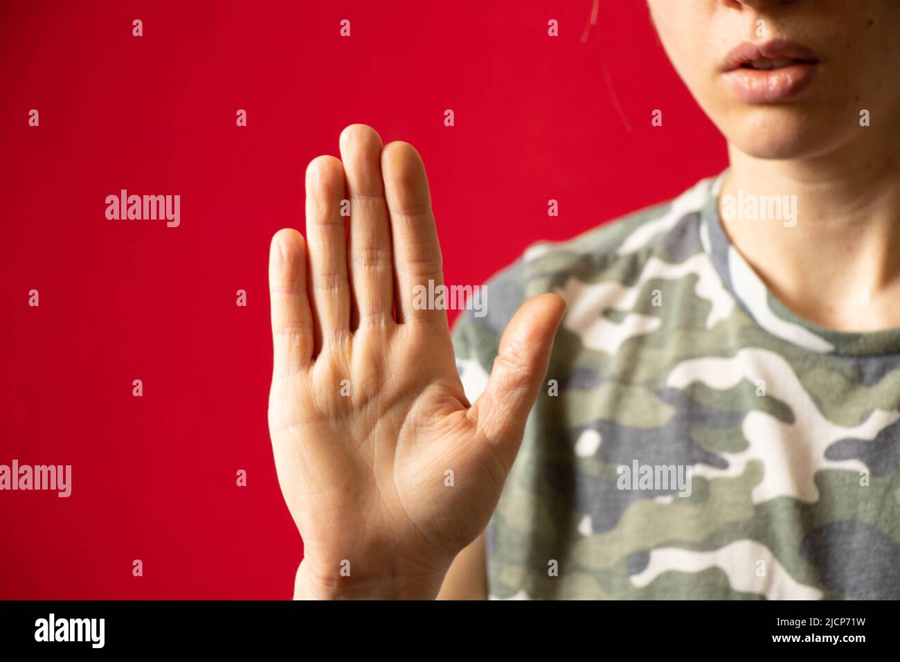 Mano di una ragazza in un uniforme mimetizzazione su uno sfondo rosso isolato primo piano, mano gesto, arresto Foto Stock