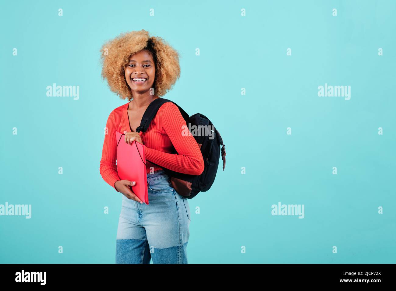 Afro studentessa donna sorridendo mentre trasportano lo zaino e tenendo una cartella su uno sfondo isolato. Foto Stock