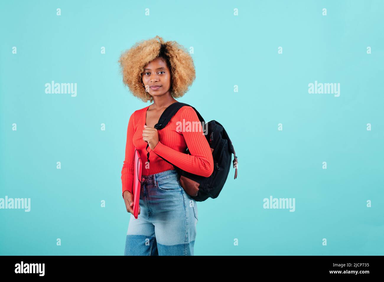 Afro studentessa donna che tiene una cartella e porta uno zaino sulla schiena mentre si trova su uno sfondo isolato. Foto Stock