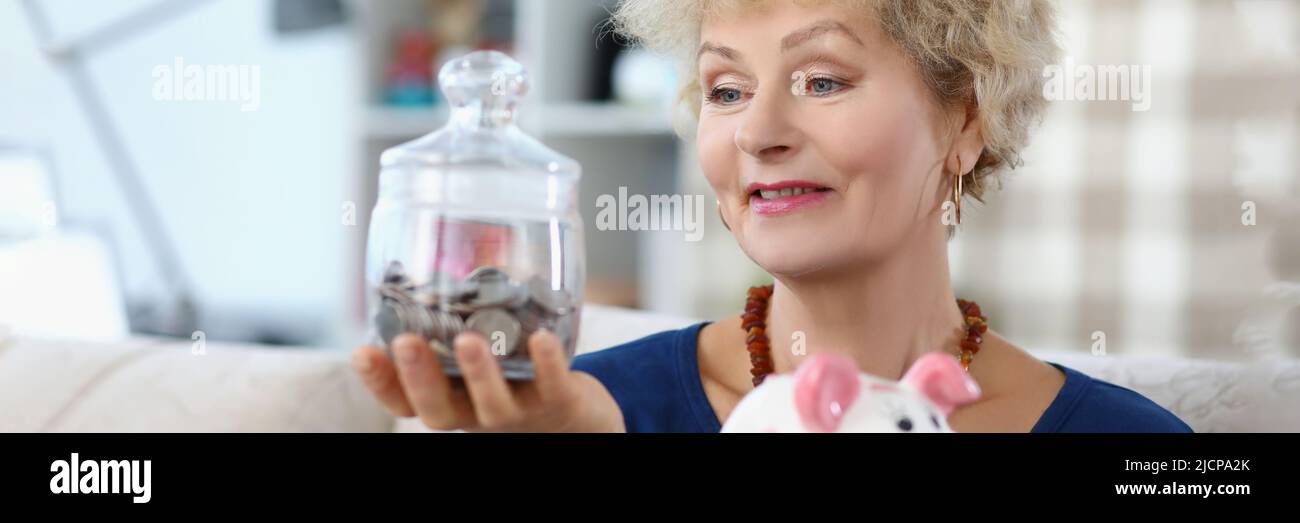 Donna anziana tenere contenitore di vetro con soldi risparmiati per la pensione Foto Stock
