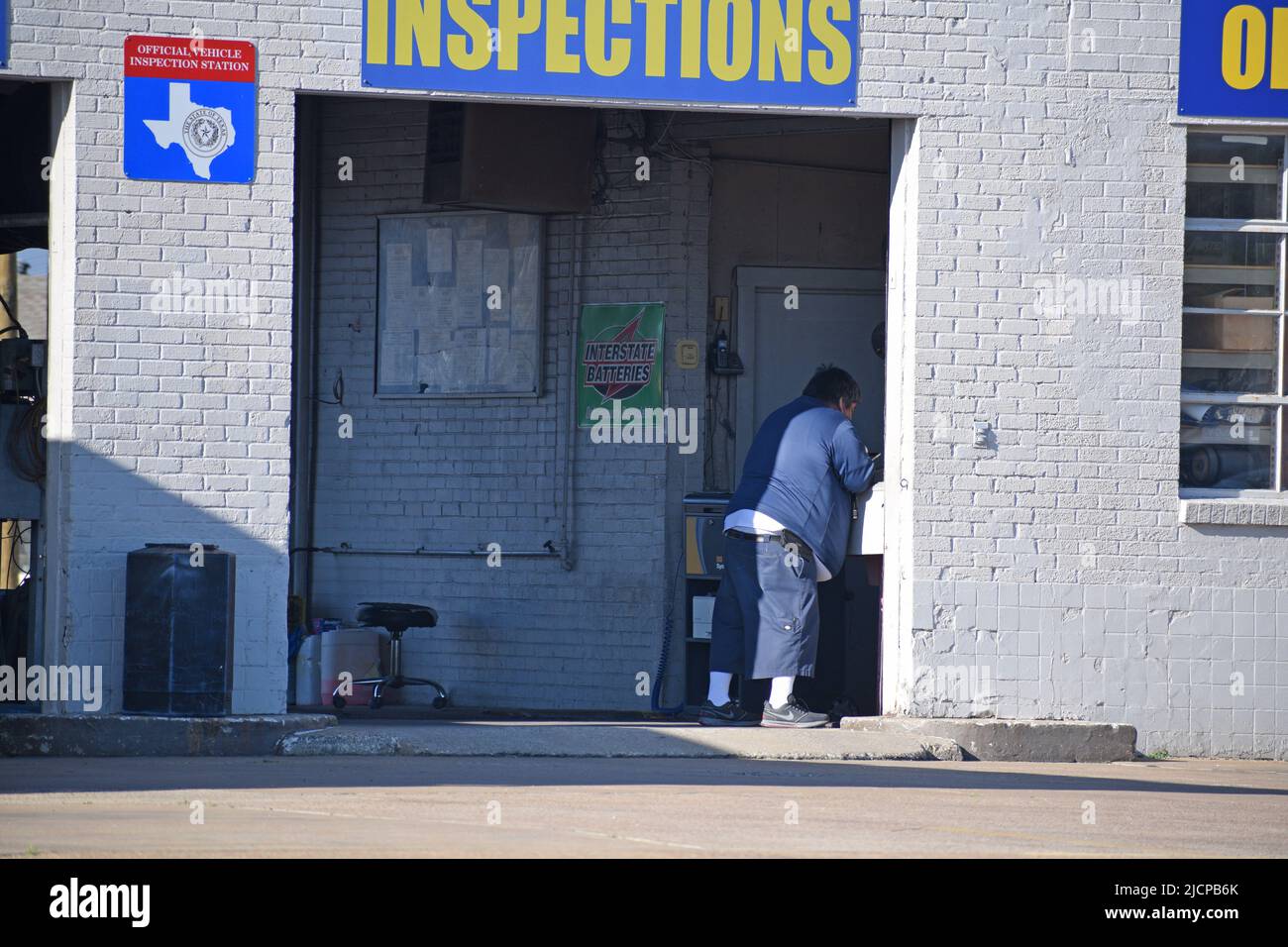 Un uomo in sovrappeso al lavoro in un negozio di riparazione auto a Irving, Texas, che fornisce anche ispezioni statali Foto Stock